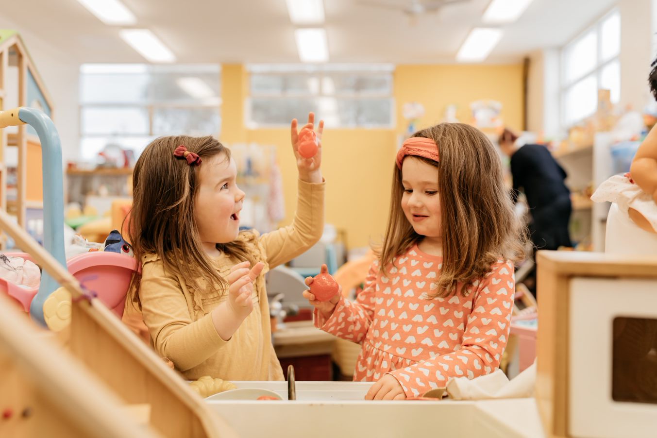 Two young girls play with a pretend kitchen sink. 