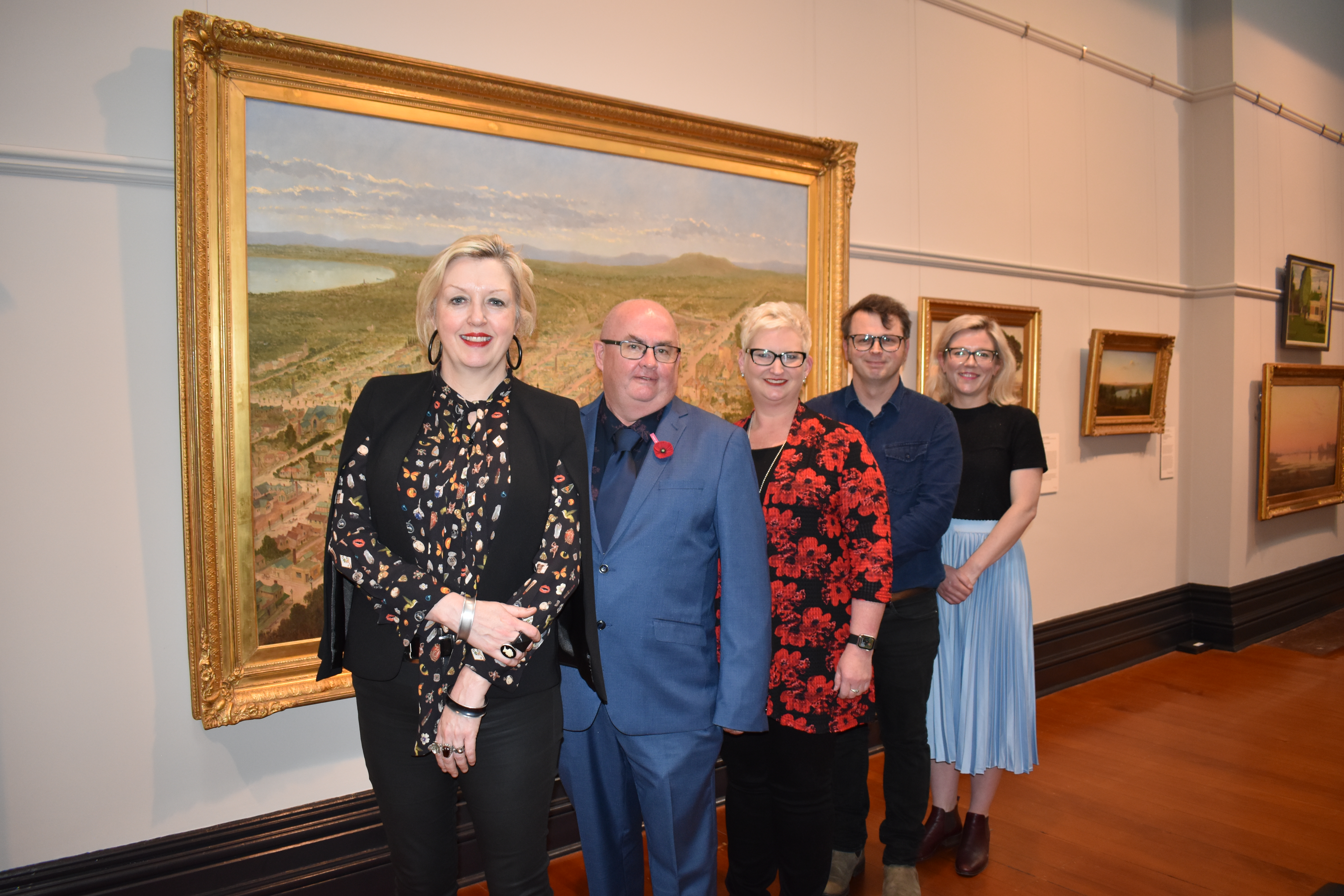 Art Gallery of Ballarat Director Louise Tegart, City of Ballarat Mayor Cr Des Hudson, ACU Campus Dean Ballarat Professor Bridget Aitchison, ACU Senior Lecturer in History, National School of Arts and Humanities Dr Benjamin Mountford and Sovereign Hill Museums Association Head of Collections and Curatorial Lauren Bourke stand in front of a large painting in a gold frame. 