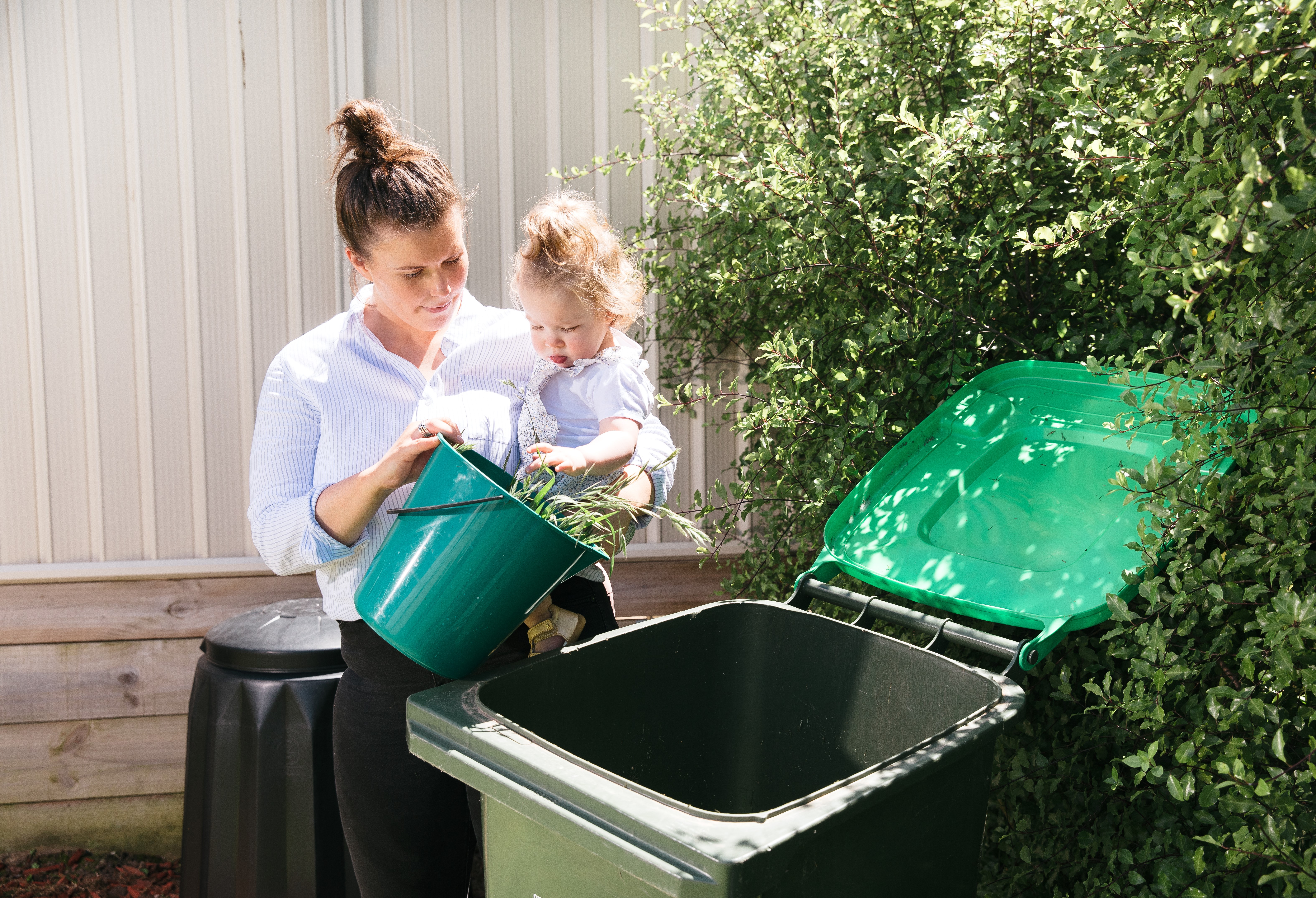 A woman and her young child tip green waste into a green lid bin. 