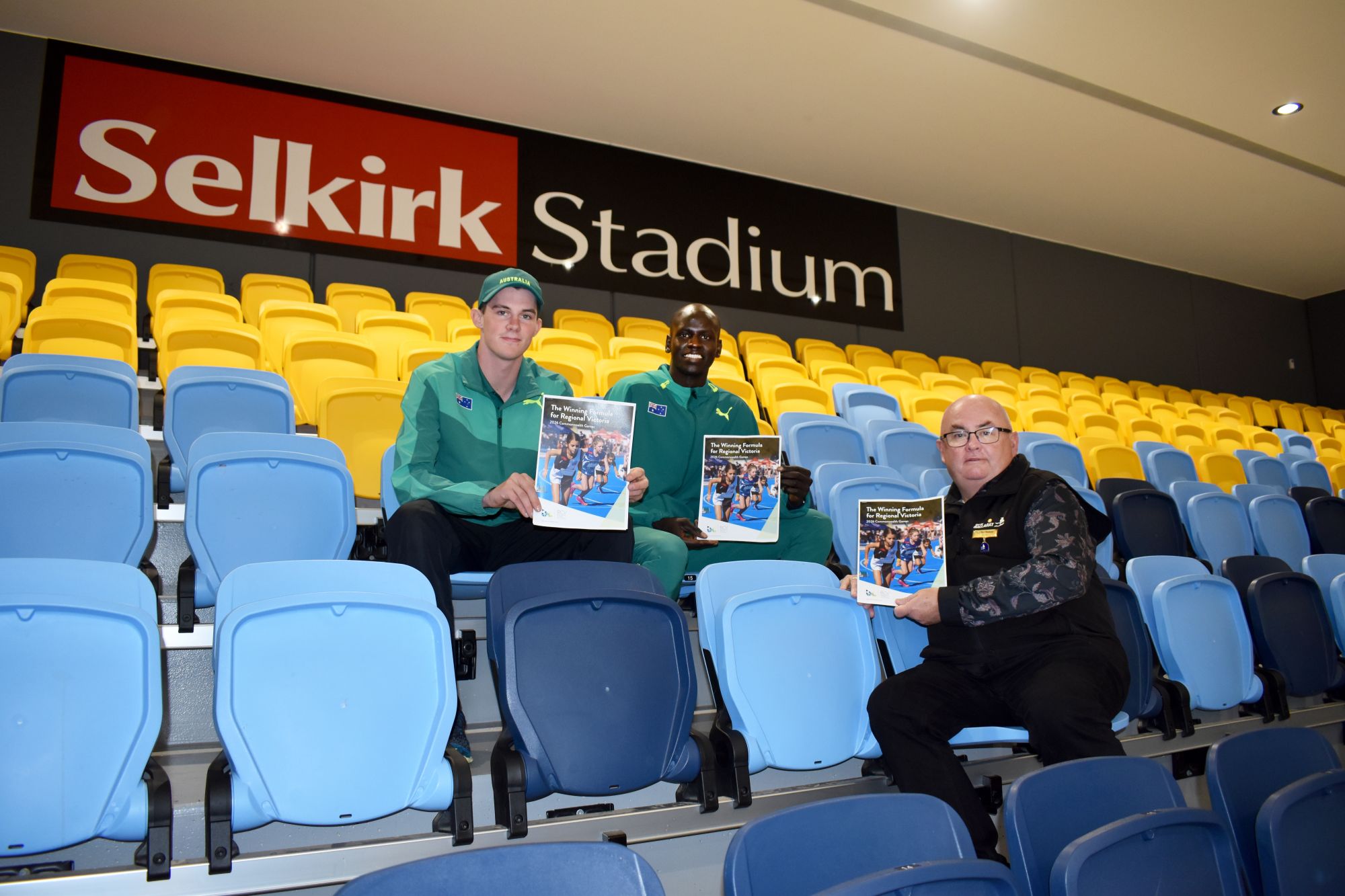 Sitting in the stands of Selkirk Stadium holding The Winning Formula document are athletes Lachlan O'Keefe and Yual Reath with Mayor Cr Des Hudson