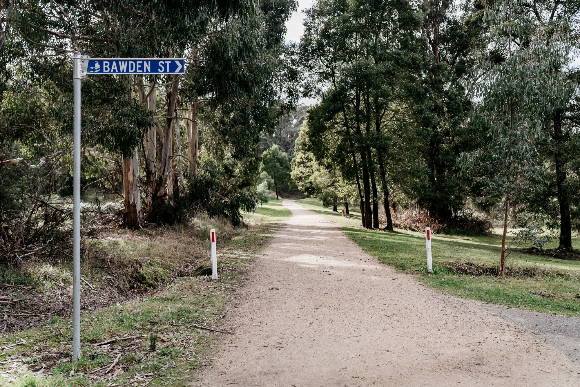 A blue sign on the left says 'Bawden Street'. Next two it there is a tree-lined track. 