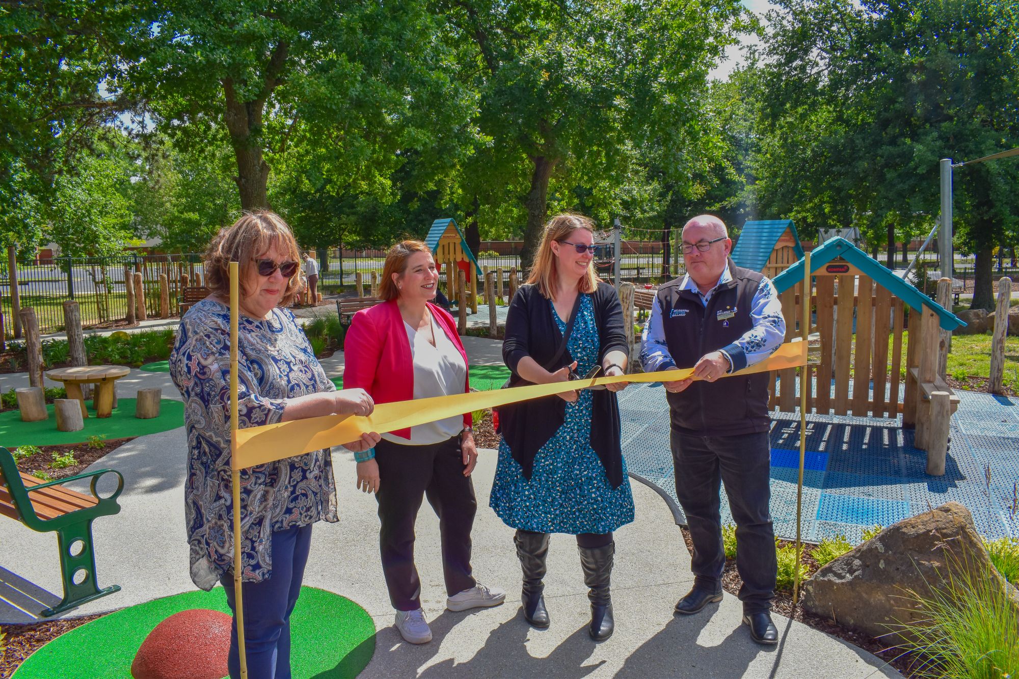 Three women and one man cut a ceremonial ribbon in front of a playground. 