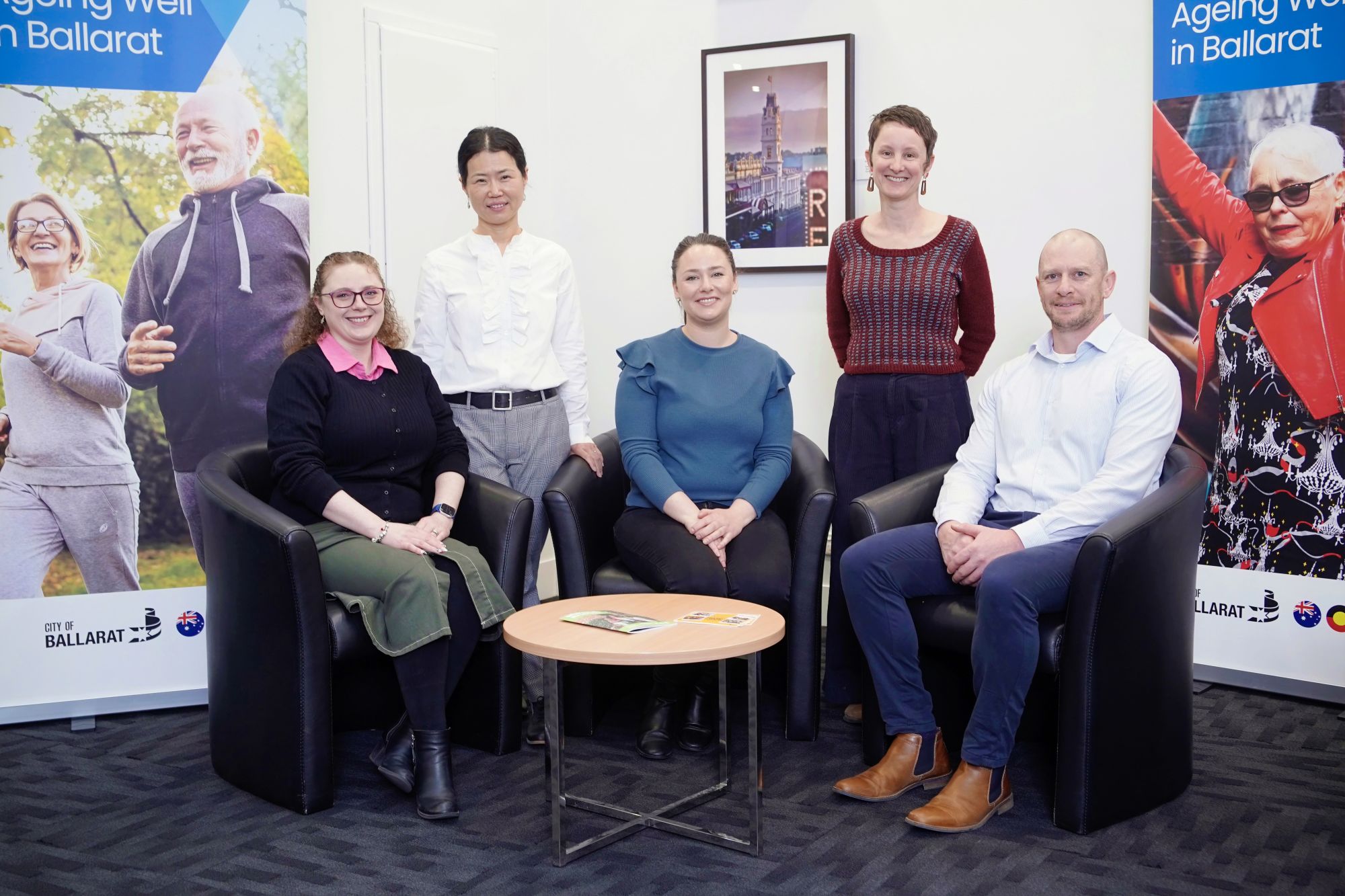 Five people, four women and one man, pose for a photo in front of banners that say 'Ageing Well in Ballarat'. 