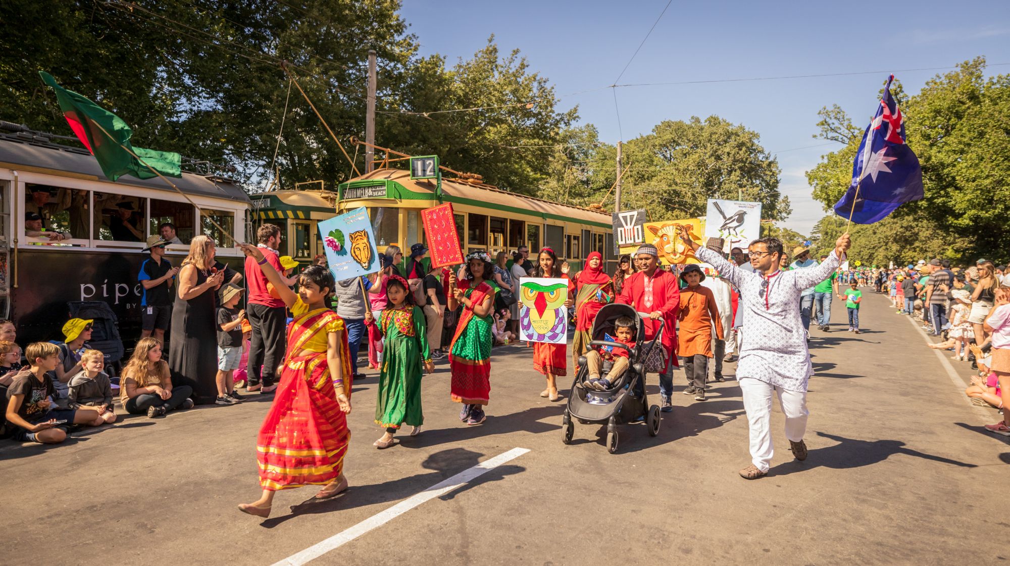 Several people in traditional cultural clothing march down the street carrying flags and banners. 