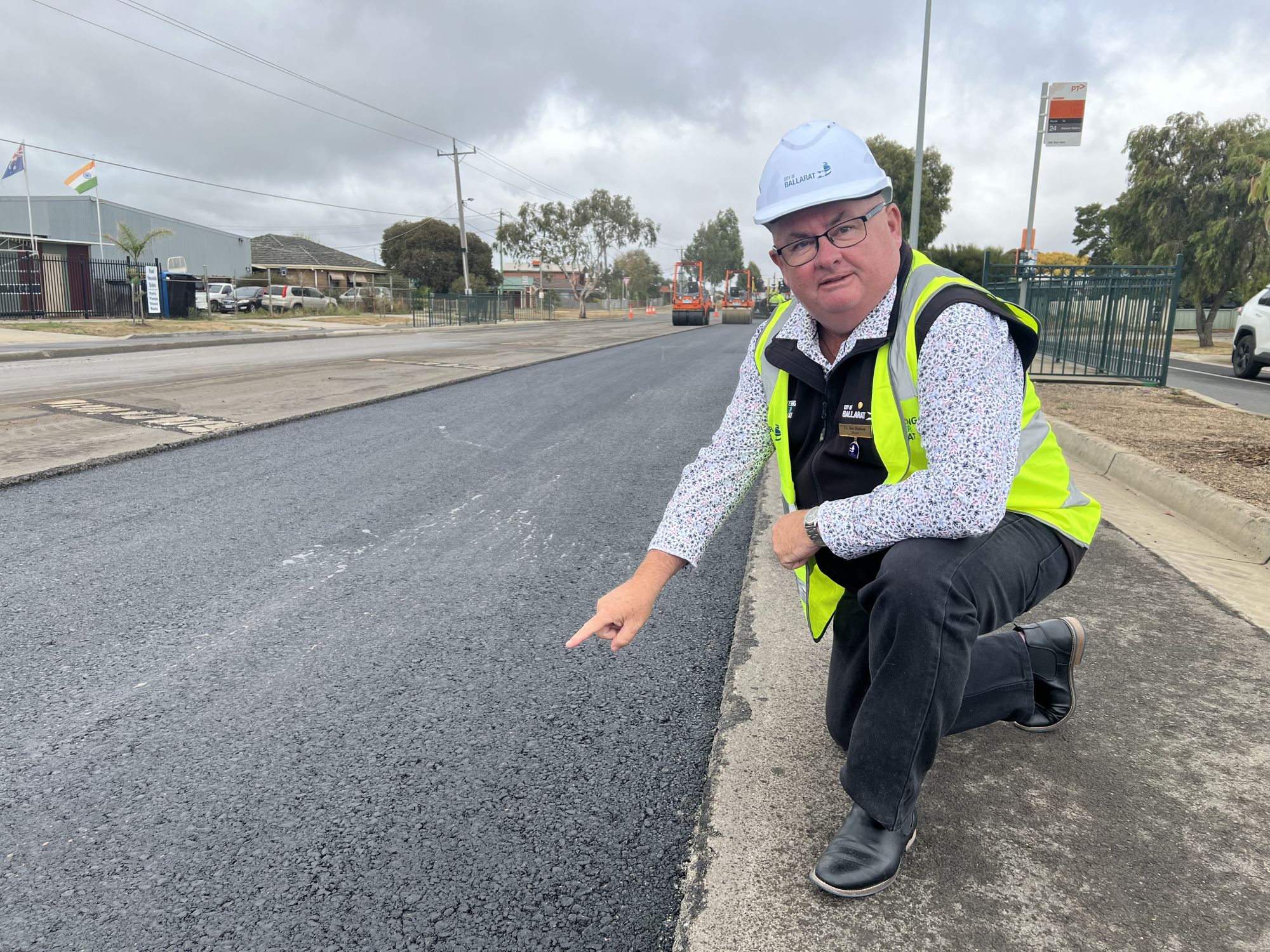 Mayor Cr Des Hudson squatting beside freshly laid road hot mix