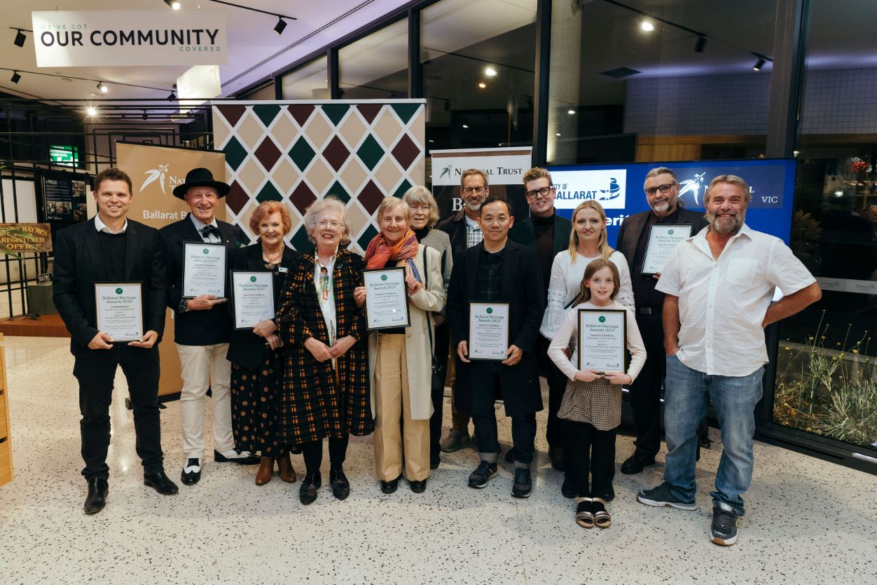 A group of people in a function centre holding certificates stand in from of several banners. 