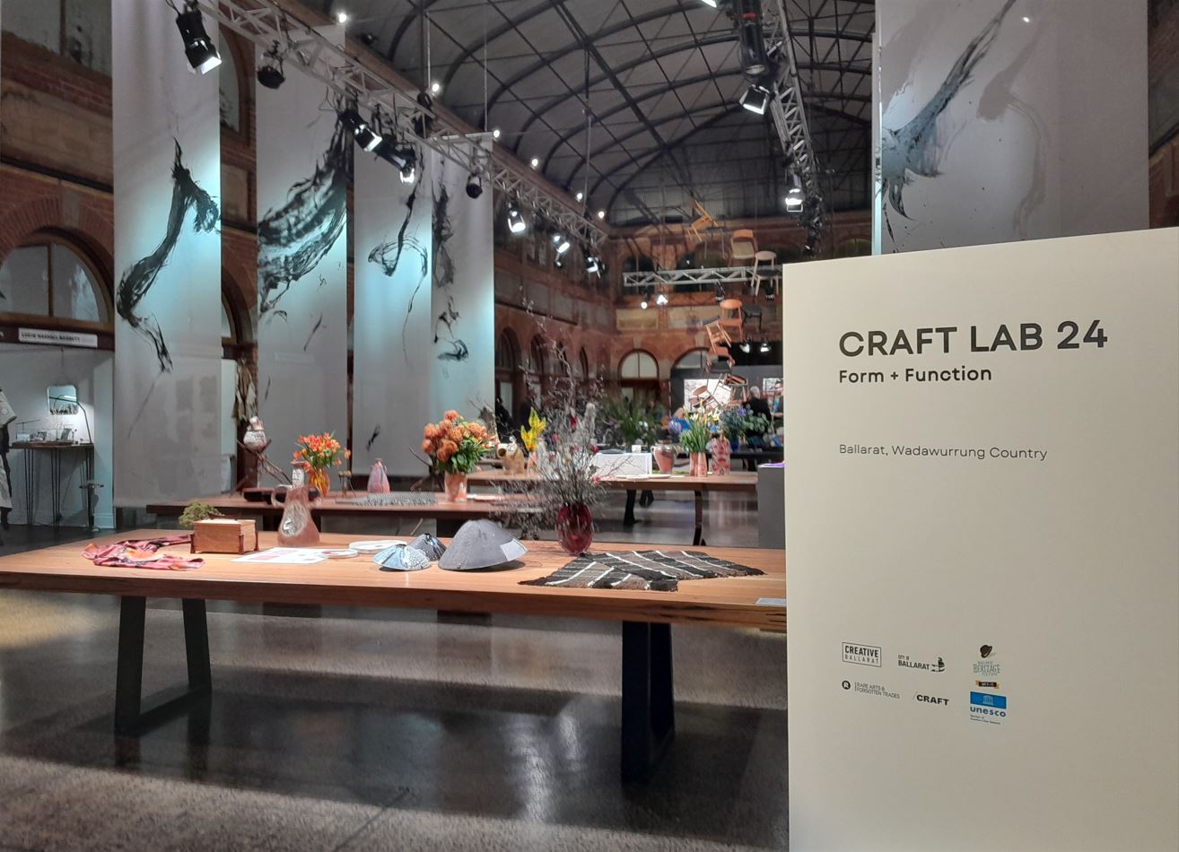 A large room with high ceilings which has wooden dining tables in it and a sign in the foreground that says 'Craft Lab 24'