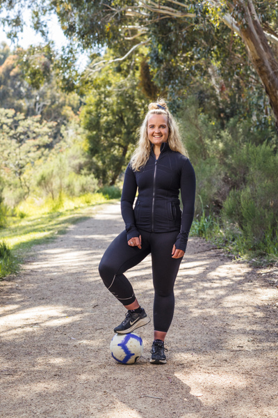 Lucy Brennan on a gravel path with one foot on a soccer ball