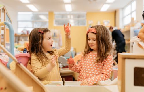 Two young girls play with a pretend kitchen sink. 