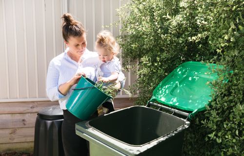 A woman and her young child tip green waste into a green lid bin. 