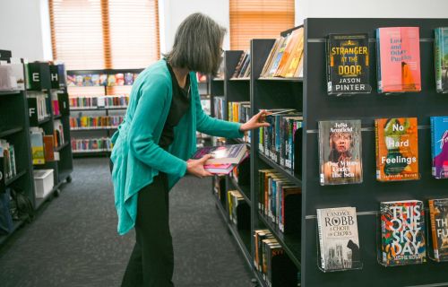 A woman in a teal cardigan arranges books on a bookshelf in the Ballarat Town Hall Library. 