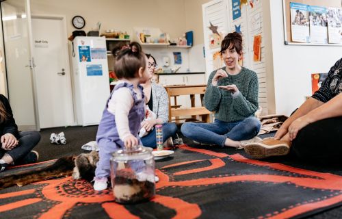 A young child looks back at their mother while sitting on a toy. 