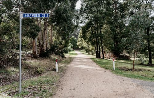 A blue sign on the left says 'Bawden Street'. Next two it there is a tree-lined track. 