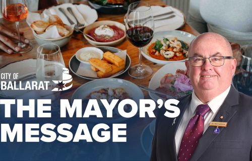 Text with The Mayor's Message with an image of Mayor Cr Des Hudson in front of a table of food and wine