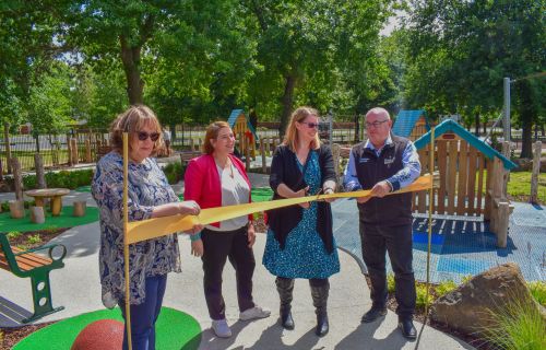 Three women and one man cut a ceremonial ribbon in front of a playground. 