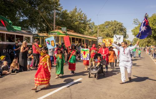 Several people in traditional cultural clothing march down the street carrying flags and banners. 