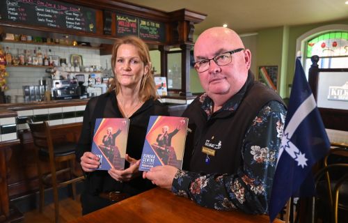 A man and woman stand in an Irish pub, holding two brochures, with a small Eureka flag on the side.