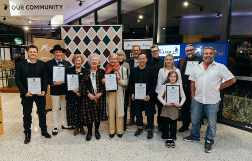 A group of people in a function centre holding certificates stand in from of several banners. 