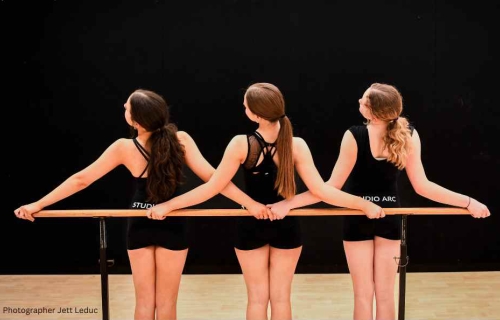 Three women face away from the camera holding onto a ballet bar.