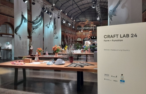 A large room with high ceilings which has wooden dining tables in it and a sign in the foreground that says 'Craft Lab 24'