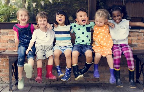 Small children smiling sitting on a bench together 