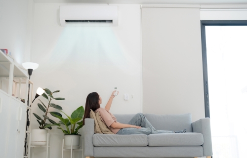 woman in a couch reach up to turn on her air conditioning with a remote control