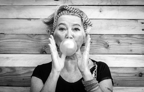 black and white photo of an older woman blowing a bubble with bubble gum