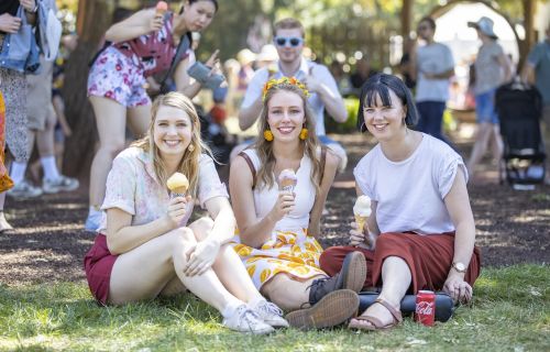 Three women sitting on the ground outside eating ice-cream