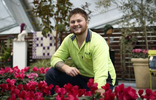 a young man kneeling in a garden bed smiling at the camera