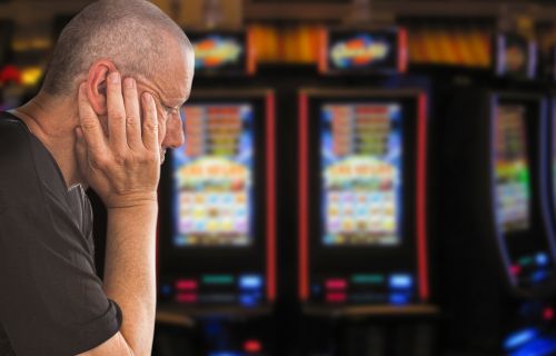 A man with head in hands with poker machines in the background