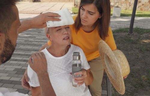 People helping mature woman on city street. Suffering from heat stroke