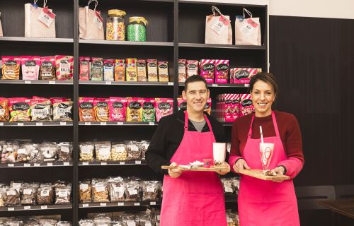 man and lady standing in front of a Darrell Lea chocolate display shelf holding milkshakes