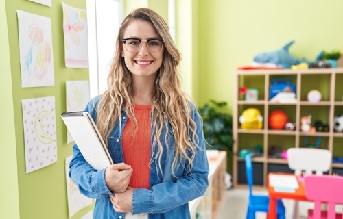 Young caucasian woman working as teacher at kindergarten looking positive and happy standing and smiling with a confident smile showing teeth