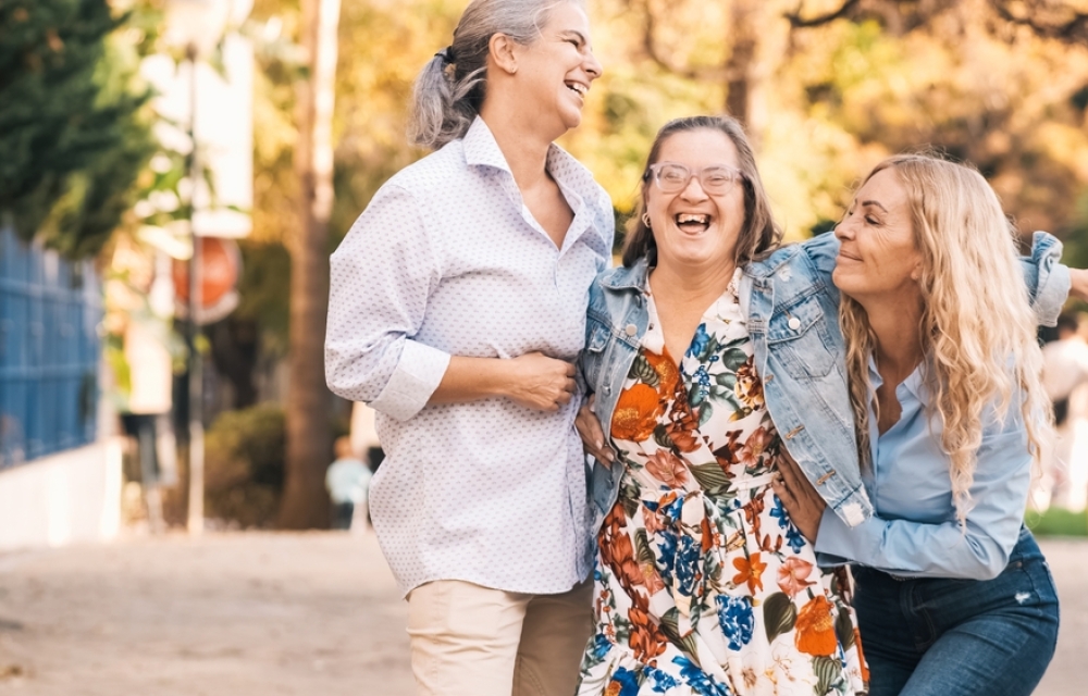 Three happy women laughing and smiling together outdoors, celebrating friendship and inclusion