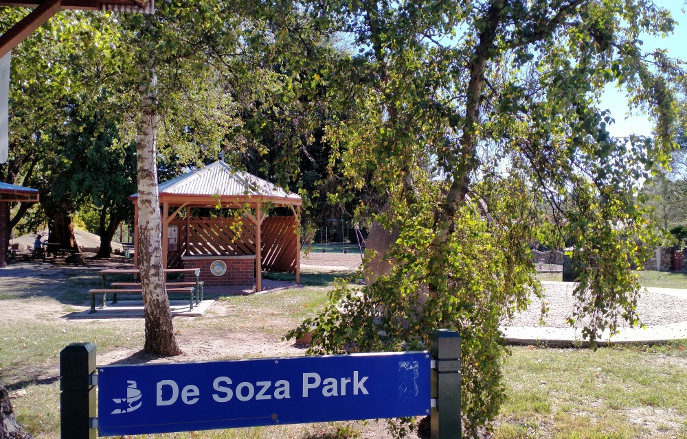 De Soza Park sign with green grass and gazebo in the background