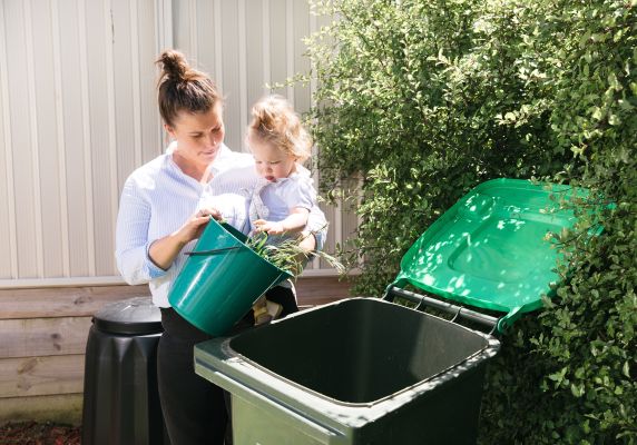 A woman and her young child tip green waste into a green lid bin.