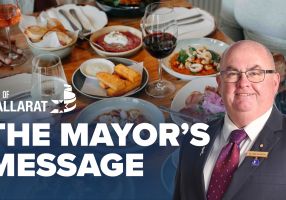 Text with The Mayor's Message with an image of Mayor Cr Des Hudson in front of a table of food and wine