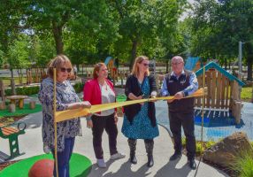 Three women and one man cut a ceremonial ribbon in front of a playground. 