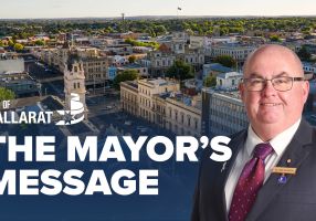 Text with The Mayor's Message with an image of Mayor Cr Des Hudson in front of an aerial shot of Ballarat
