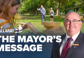 Text with The Mayor's Message with an image of Mayor Cr Des Hudson in front of a picnic in a park
