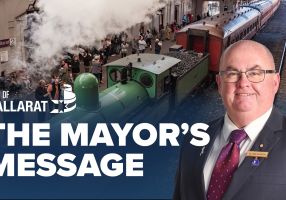Text with The Mayor's Message with an image of Mayor Cr Des Hudson in front of a steam train at Ballarat station