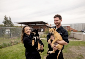 Photo of two staff members standing outside the Animal Shelter holding a puppy each and smiling