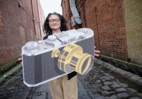 A woman holding a large cardboard cutout of a camera in a Ballarat laneway