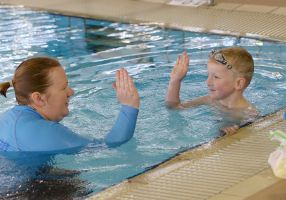 Swim teacher high fives student in pool
