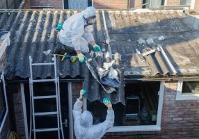 Image of professional asbestos removal: people in protective suits are removing asbestos cement corrugated roofing