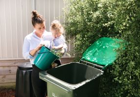Image of mother and baby placing weeds in the kerbside green waste bin