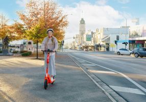 A young woman riding a bright orange e-scooter on Sturt Street with the town hall and Ballarat city in the background