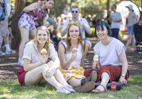 Three women sitting on the ground outside eating ice-cream