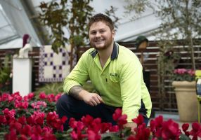 a young man kneeling in a garden bed smiling at the camera
