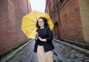 A woman stands in a laneways holding a bright yellow umbrella